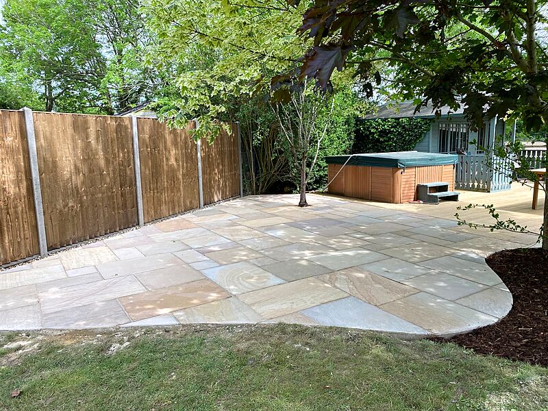 Curved sandstone patio joining timber decking with a hot tub and summerhouse