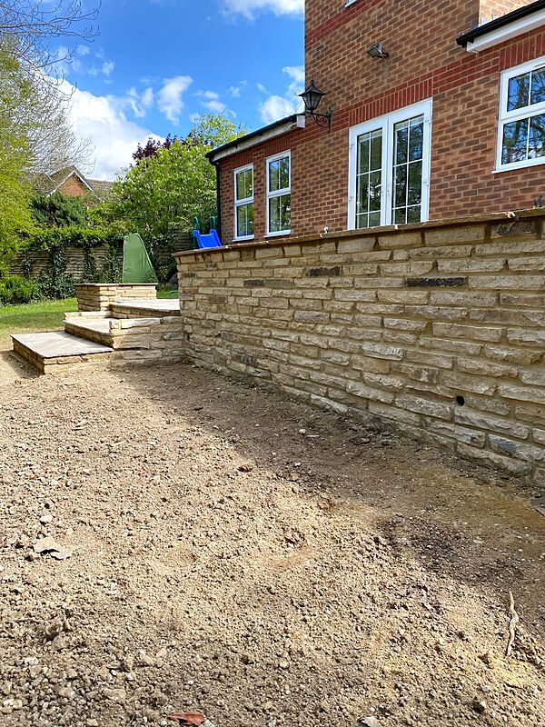 Natural stone retaining wall with sandstone coping beside a brick house