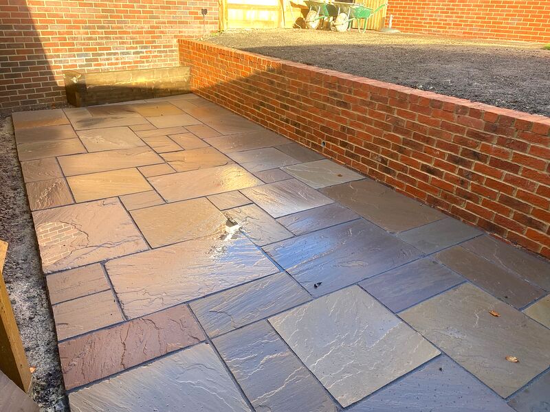 Sandstone patio laid below a newly built red brick retaining wall