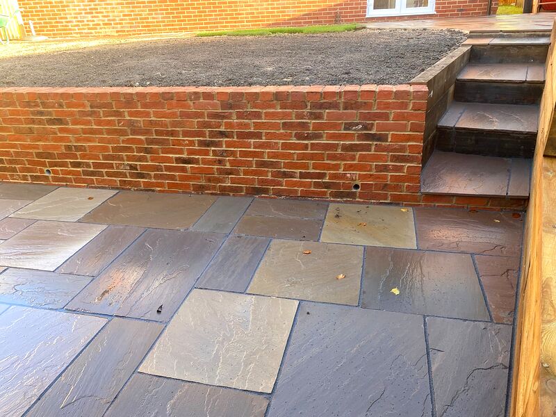 Red brick garden retaining wall with sandstone paved steps up to a lawn
