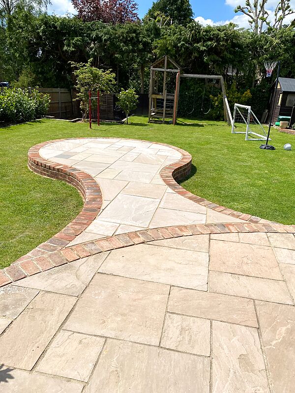 Sandstone paving circle and curved path edged with reclaimed brick set into a lawn