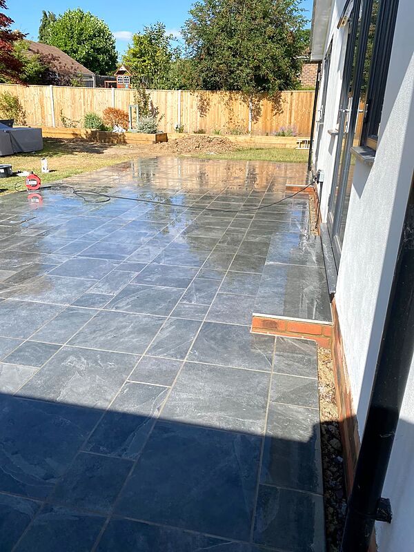 Grey tiled patio with a brick edging detail beside a rendered house