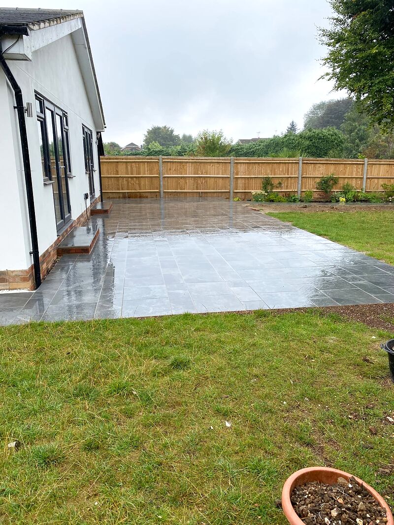 Grey paved terrace beside a white bungalow with new close-board fencing and lawn