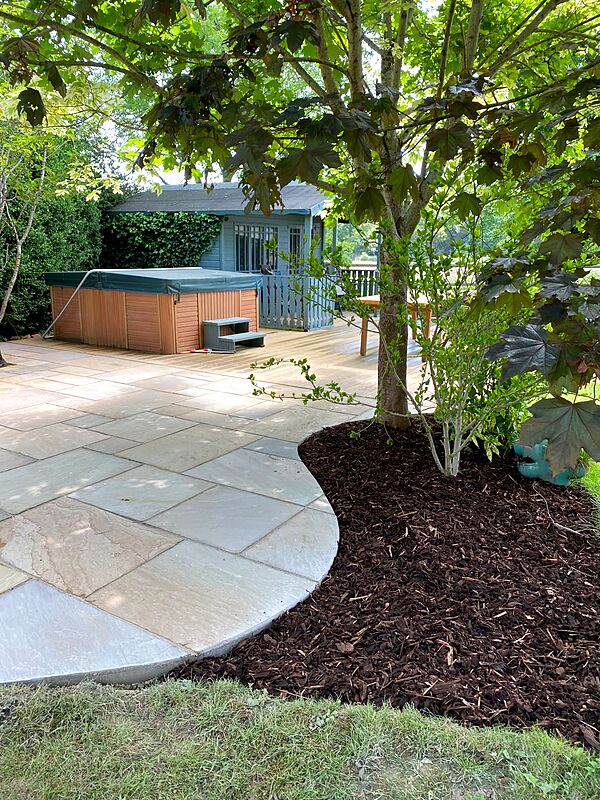 Curved sandstone patio edge beside a mulched planting border and mature tree
