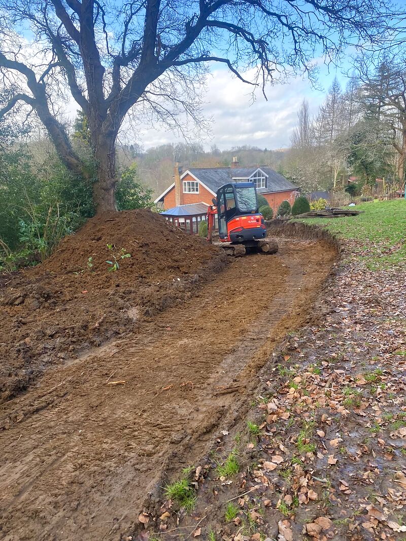 Mini digger excavating and levelling ground for a new driveway beside a country house