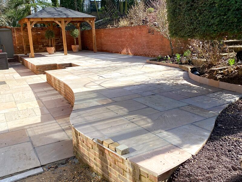 Curved brick retaining wall with sandstone coping beside a large sandstone terrace