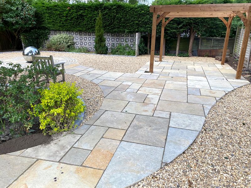 Curved sandstone paved path leading across a gravel garden to a timber pergola