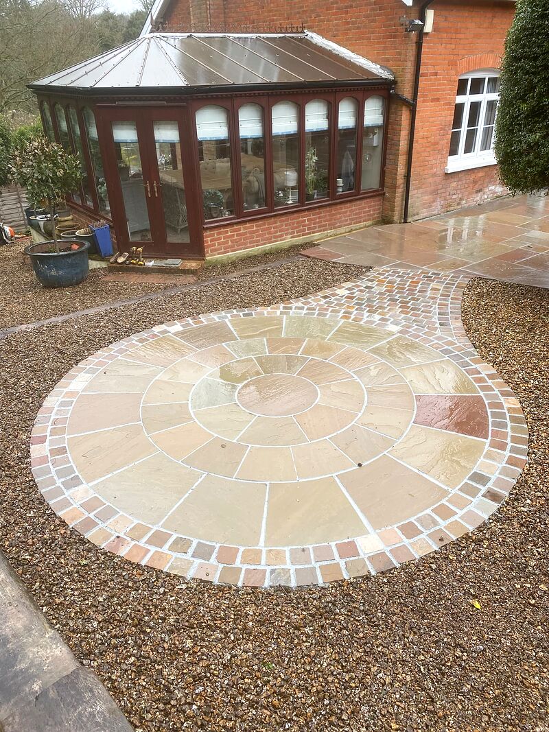 Sandstone paving circle with brick sett edging and a curved cobbled path beside a conservatory