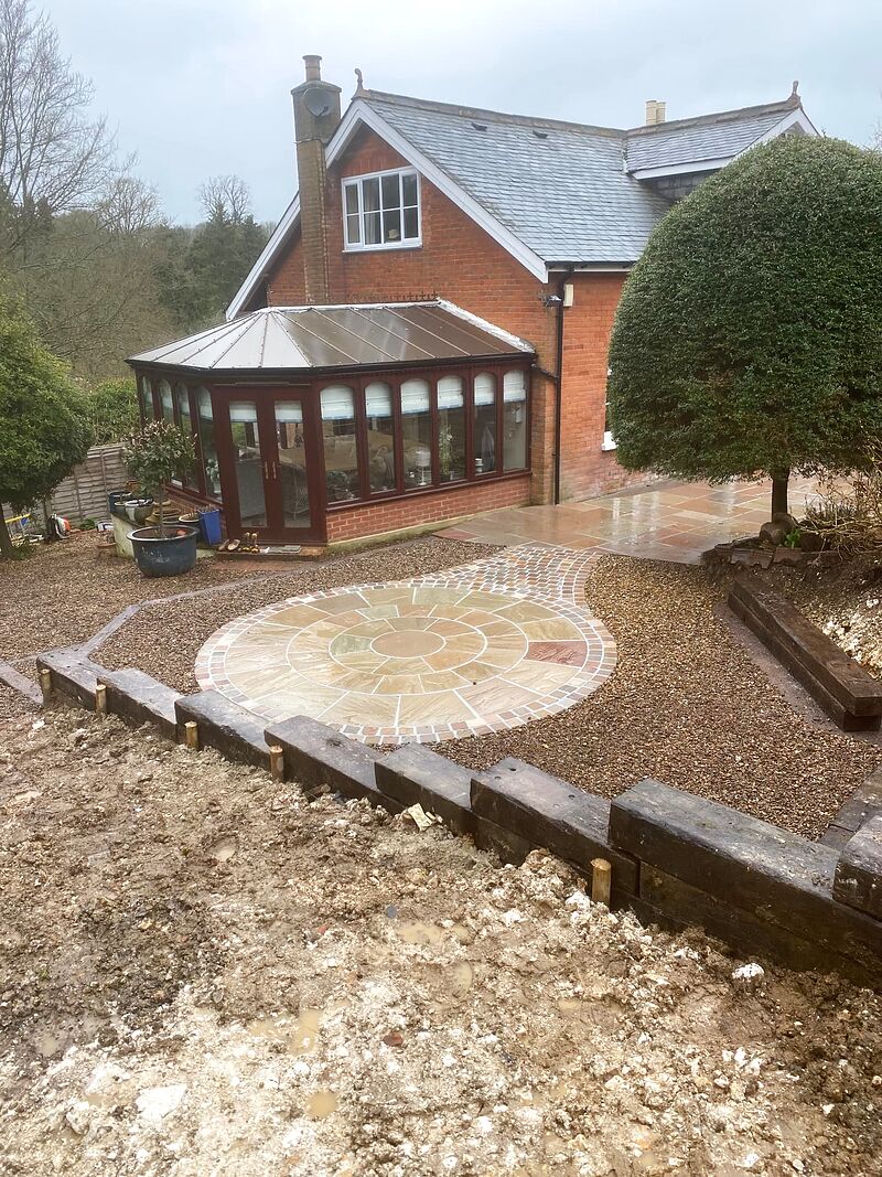 Sandstone paving circle with brick surround set into gravel beside a conservatory
