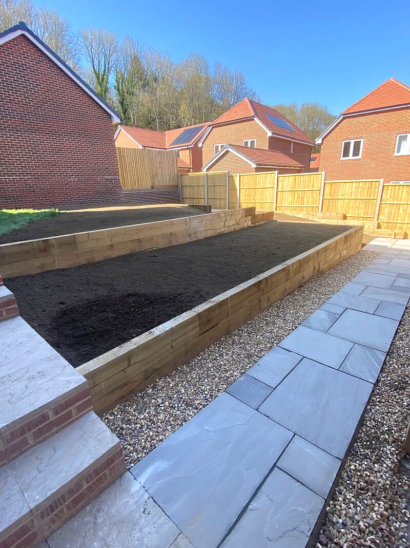 Grey sandstone path with brick steps beside timber sleeper raised beds filled with topsoil
