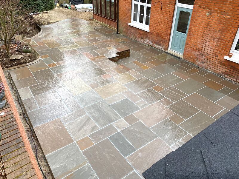 Sandstone paving laid around a side entrance of a red brick house with a drainage channel