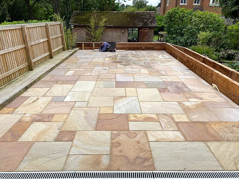 Large mixed-size sandstone patio framed by timber sleeper retaining walls