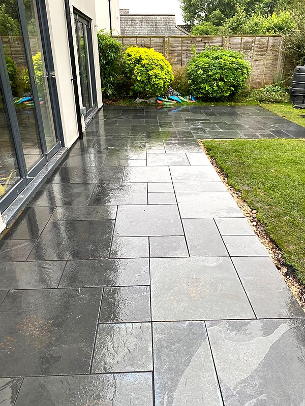 Dark slate grey patio laid beside bi-fold doors with a gravel margin to the lawn