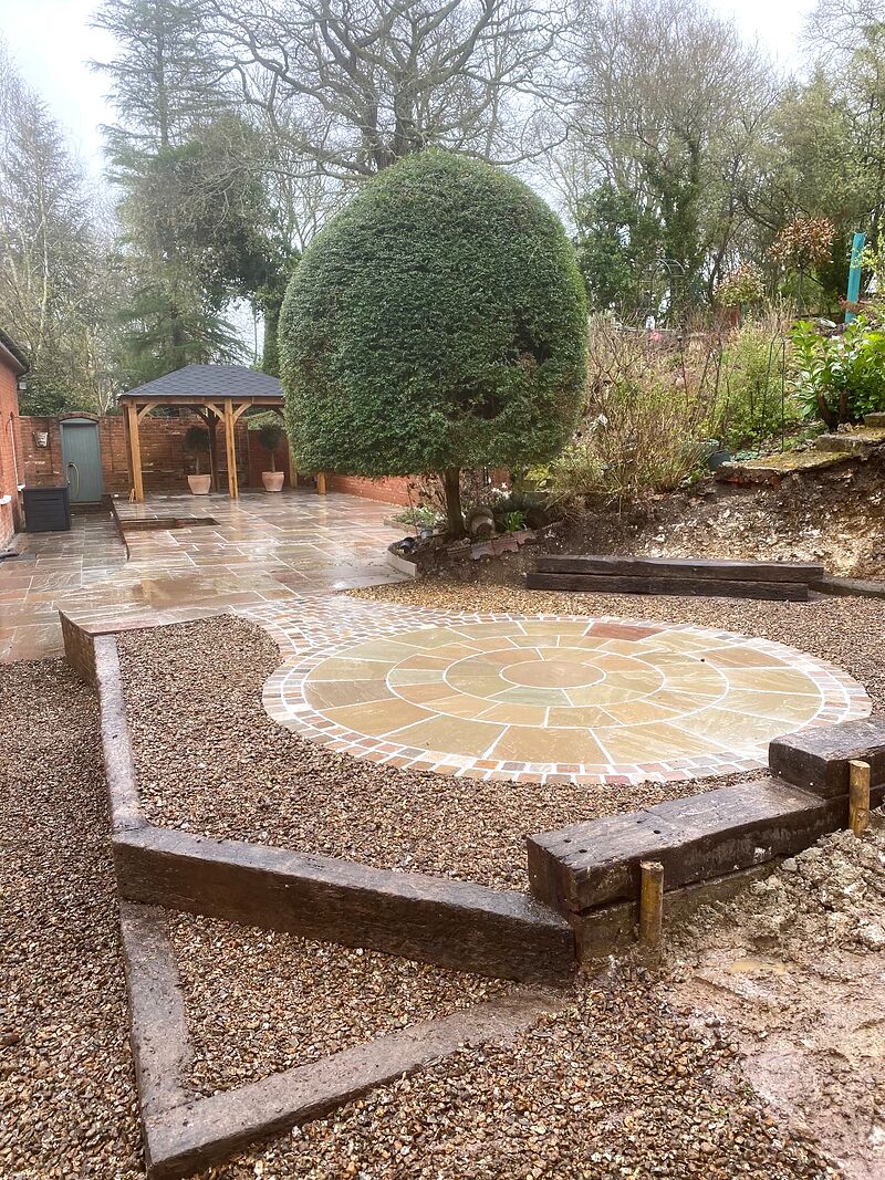 Sandstone paving circle in gravel with a wider terrace and oak gazebo beyond