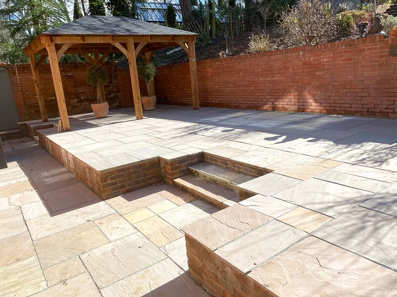Sandstone terrace on two levels in a brick walled garden with an oak gazebo