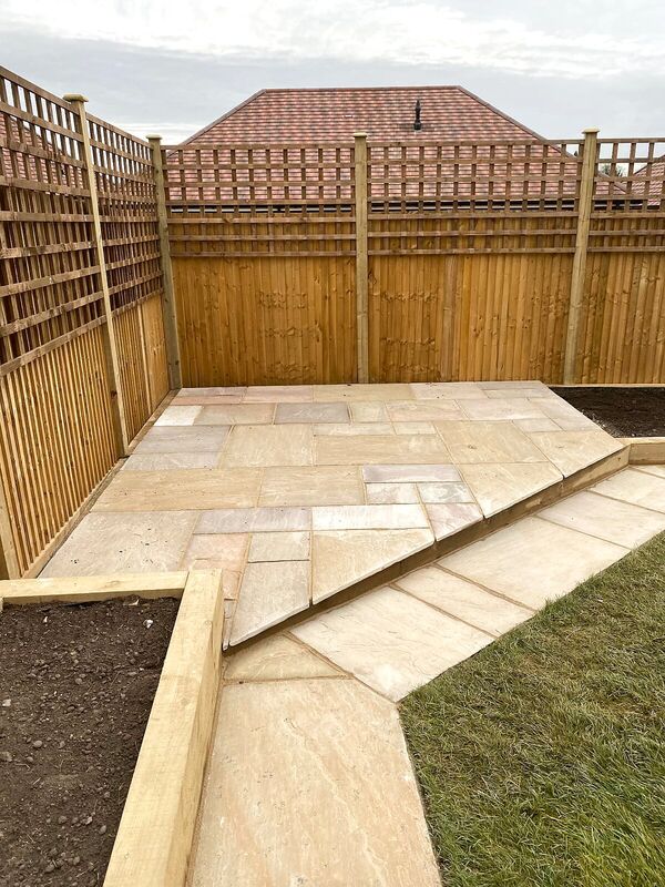 Sandstone corner patio enclosed by close-board fencing with trellis tops