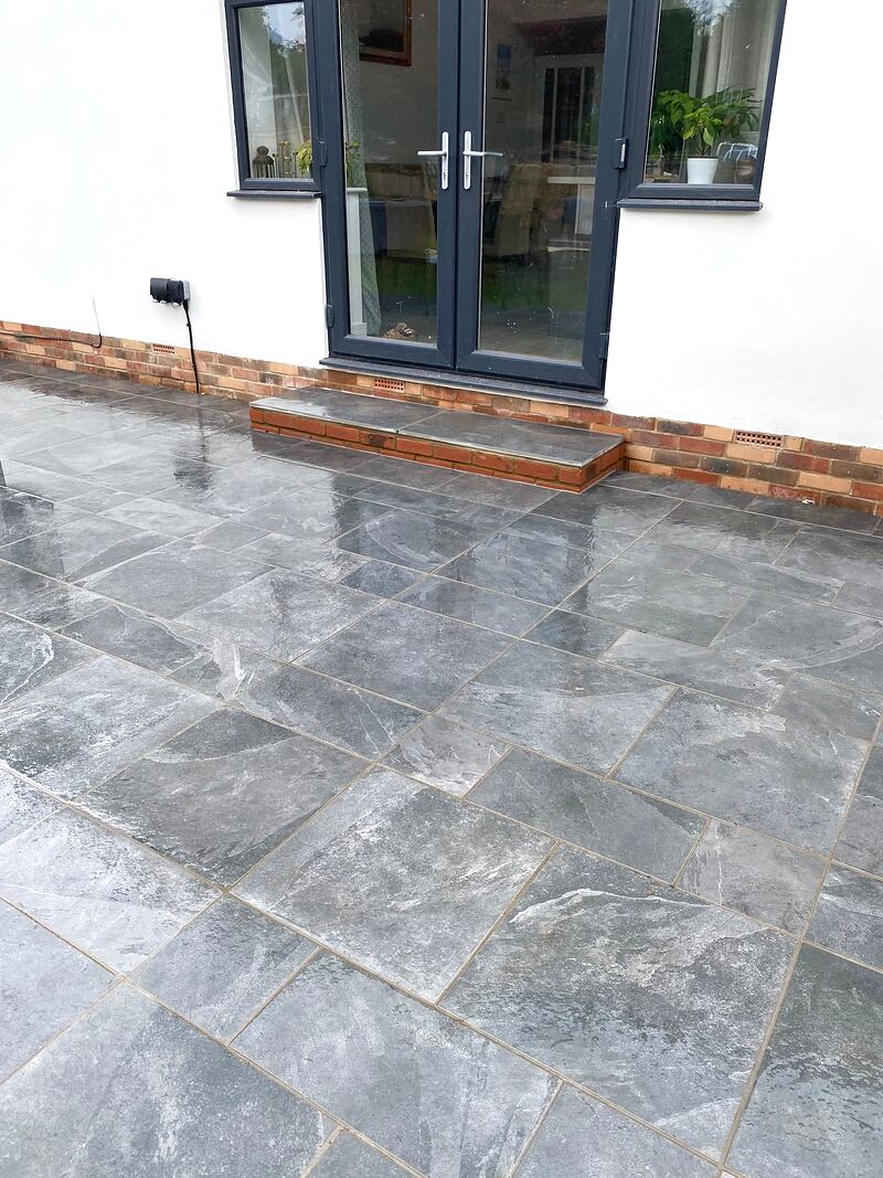 Grey slate paving laid up to French doors with a brick step in a British garden