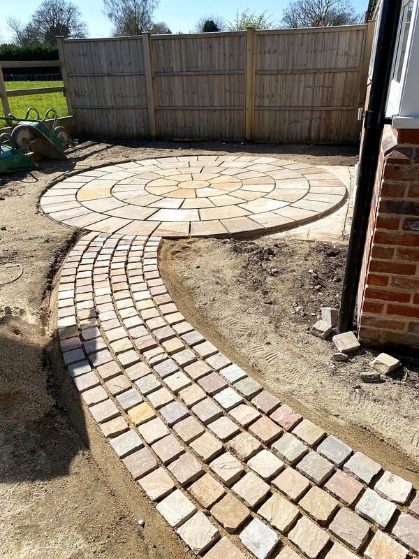 Circular sandstone paving feature with a curved setts path being laid in a garden