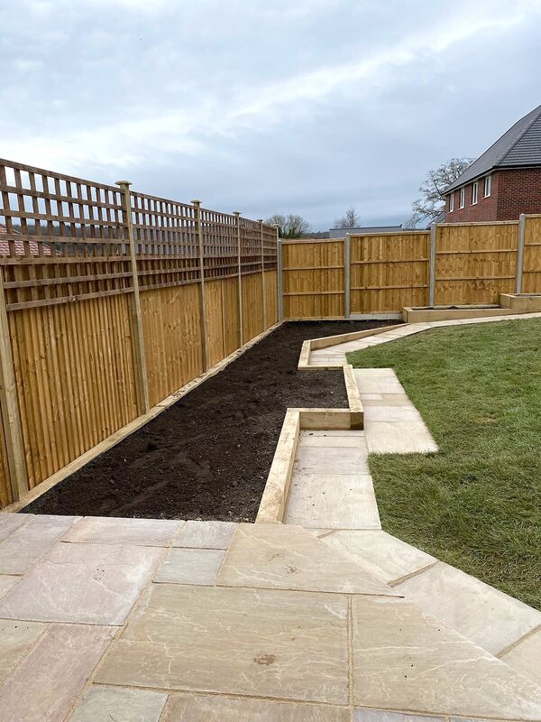 Paved garden path with sleeper edging beside a prepared planting border and new fencing